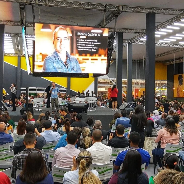 Roberto Calderon no palco principal, com o telão atrás e a plateia lotada